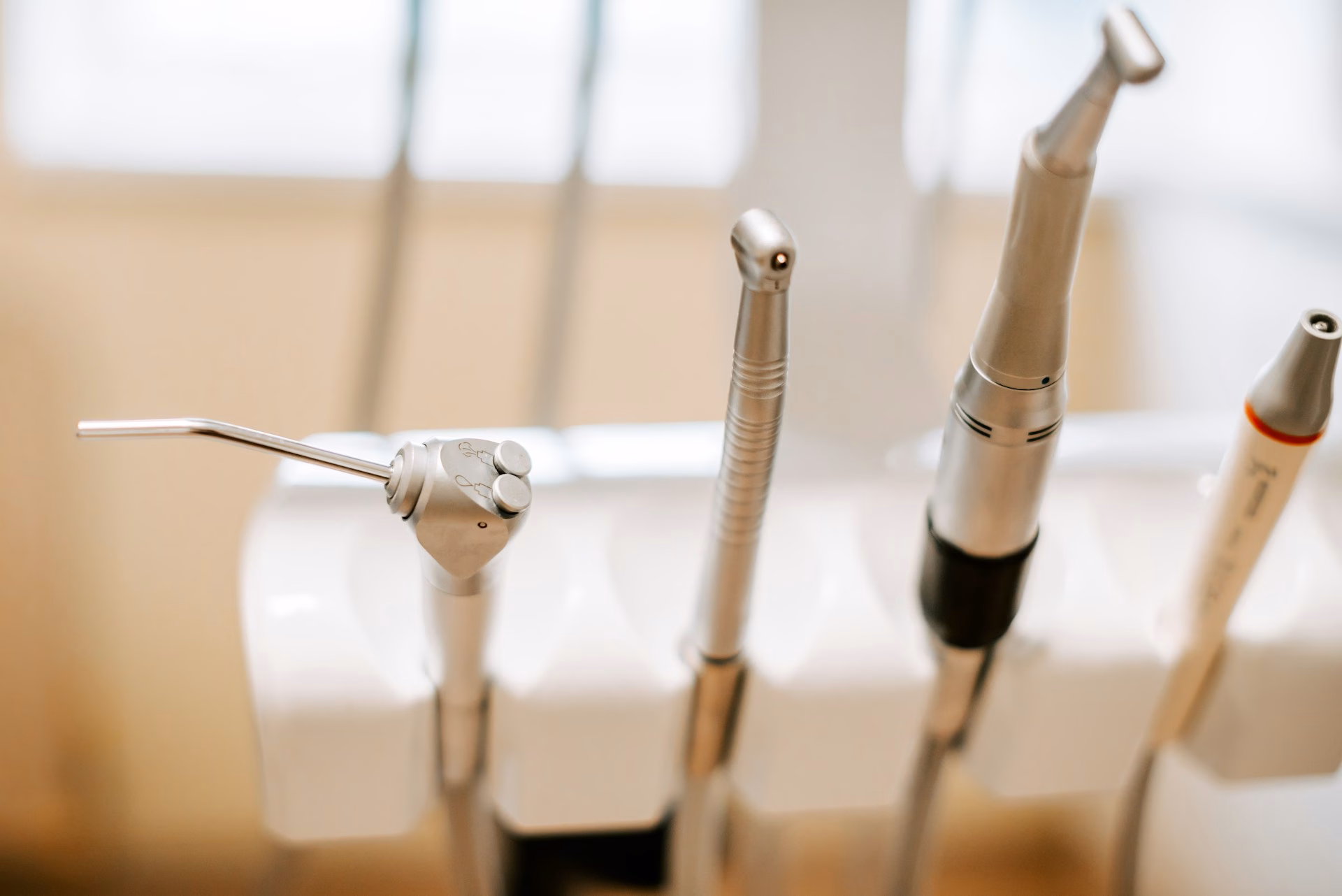 A close-up of various dental tools and instruments arranged in a holder at a dentist’s office, with a blurred background.